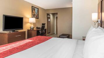 Quarto de hotel com cama, televisão, secretária com cadeira, luminária e espelho.