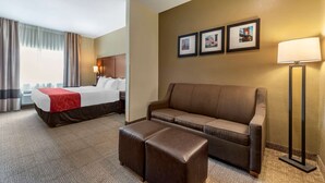 A hotel room with a bed, a brown sofa, a small ottoman, and a floor lamp. There are three framed pictures on the wall. - Comfort Suites Mason near Kings Island (Mason)