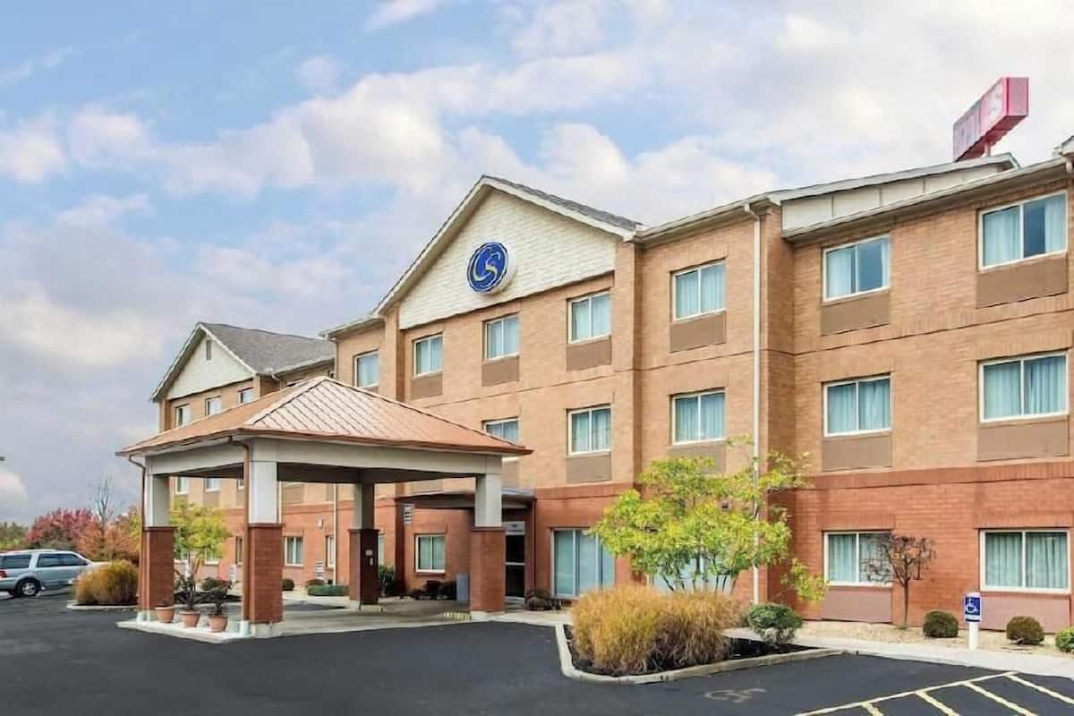 A multi-story hotel with a covered entrance, a wheelchair accessibility sign, and a parking lot.