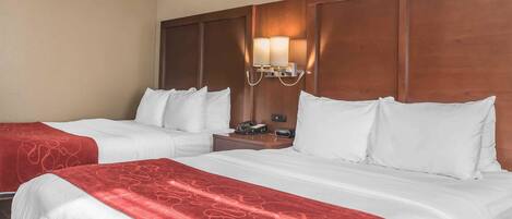 Habitación de hotel con dos camas, cabecera de madera, mesita de noche y lámpara fijada a la pared.