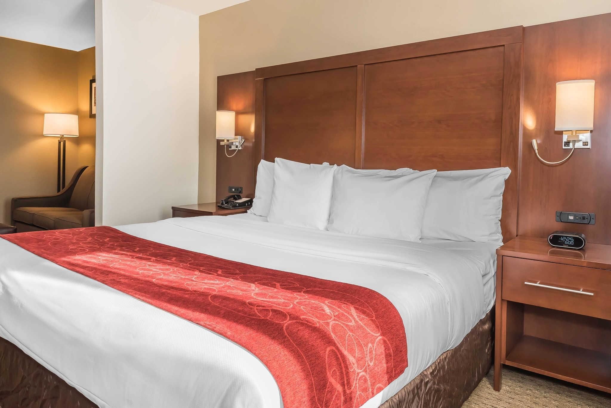 Quarto de hotel com uma cama grande, cabeceira de madeira, mesas de cabeceira com abajures e um cobertor vermelho.