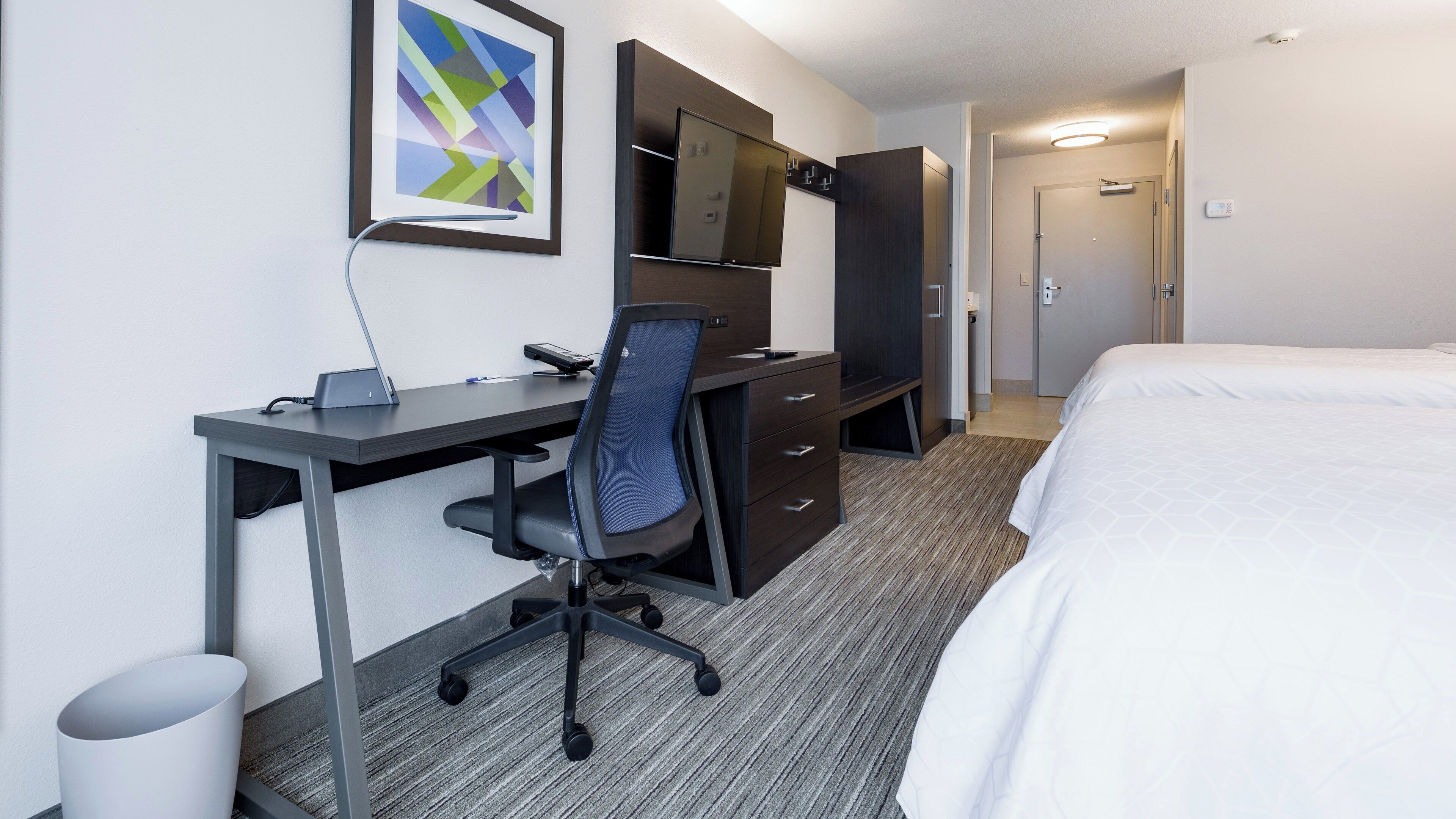 A hotel room with a desk, chair, bed, and a television on the wall.