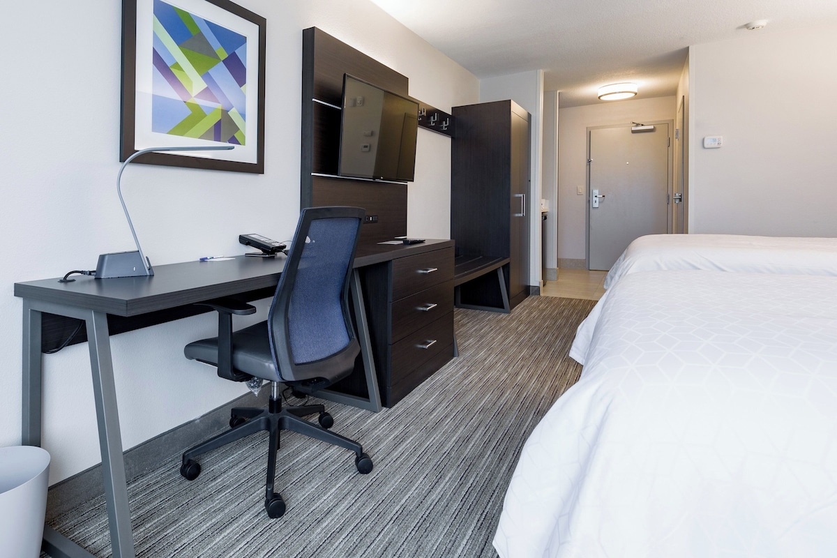 Une chambre d’hôtel équipée d’un bureau, d’une chaise, d’un lit et d’un téléviseur fixé au mur.
