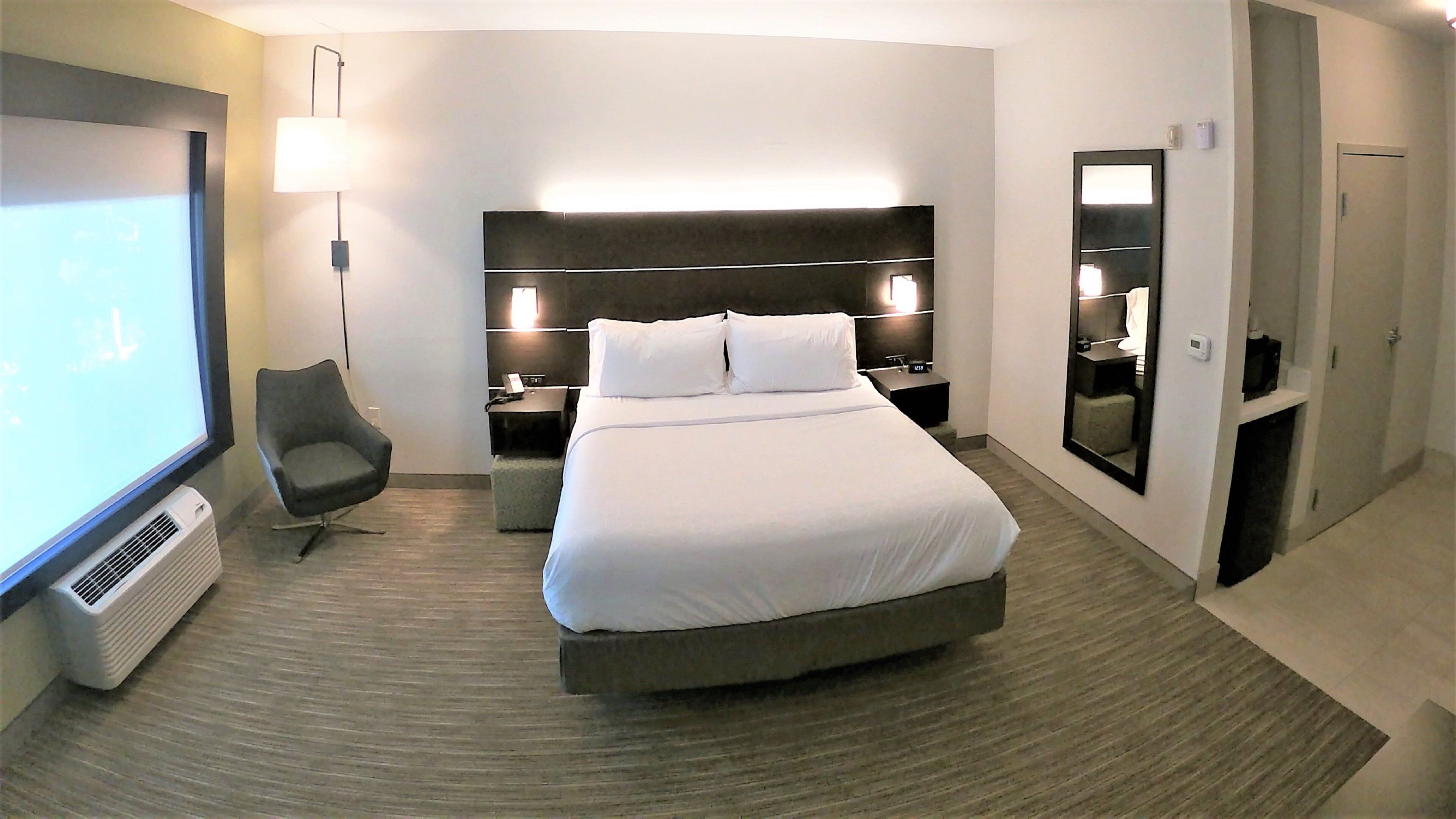 Een hotelkamer met een groot bed, een bureau, een stoel, een televisie en een spiegel.