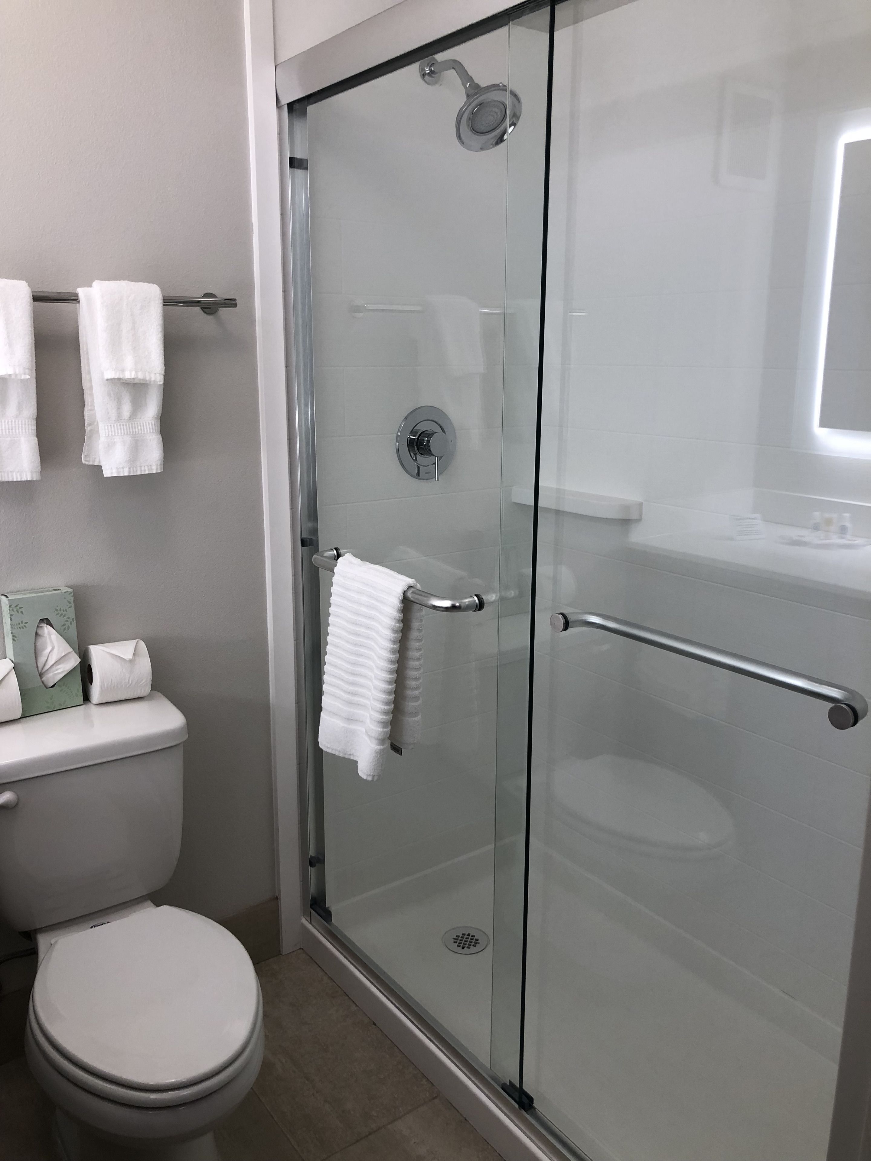 Un baño moderno con ducha de vidrio, inodoro y lavamanos con espejo.