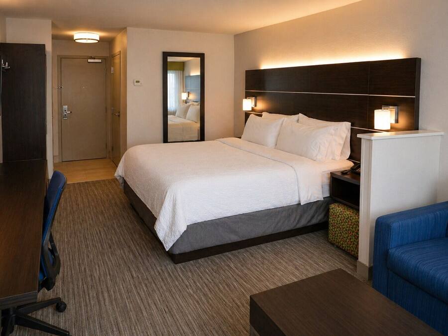 A hotel room with a bed, bedside tables, a desk, a chair, a TV, and a mirror.