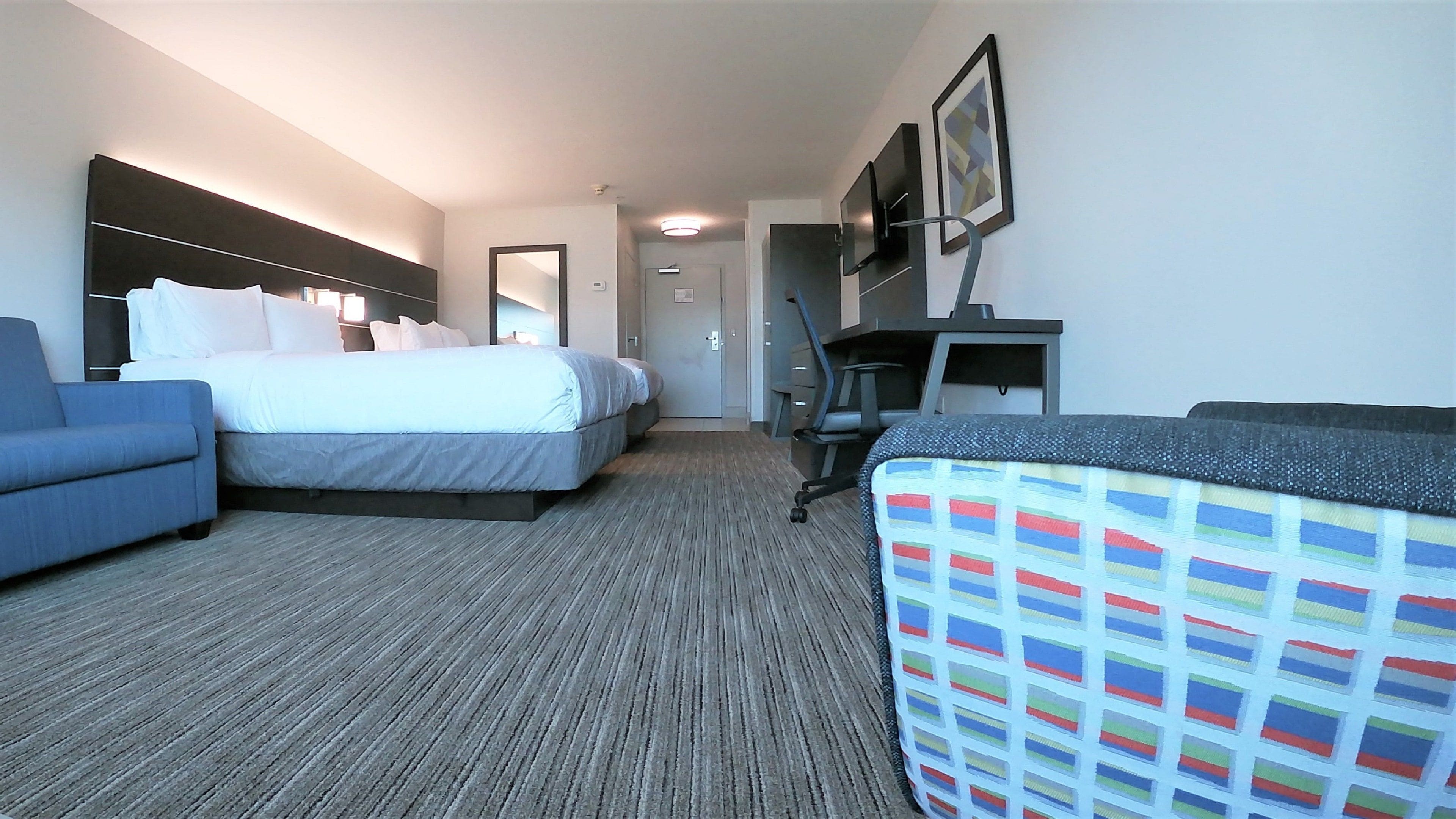 A hotel room with two beds, a desk, a chair, and a TV.