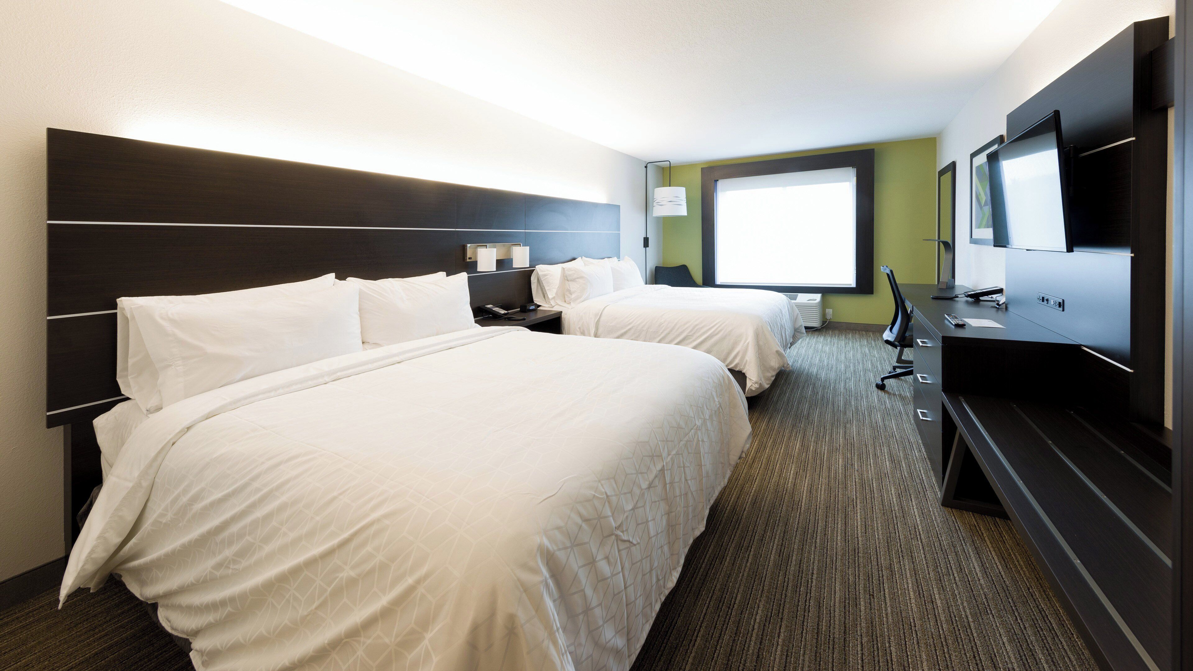 A hotel room with two beds, a desk, a TV, and a window.