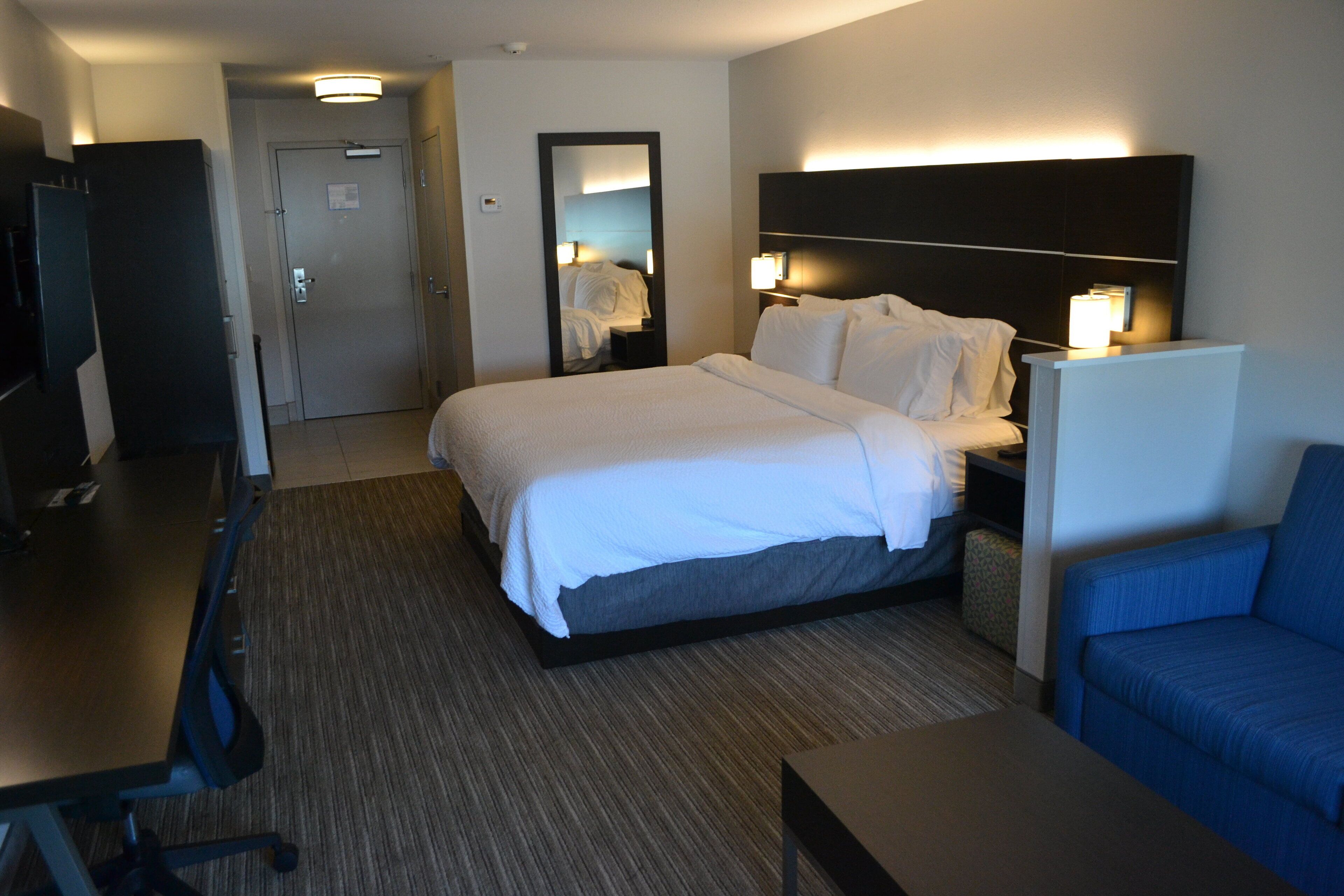 A hotel room with a large bed, a desk, a TV, a blue sofa, and a mirror.