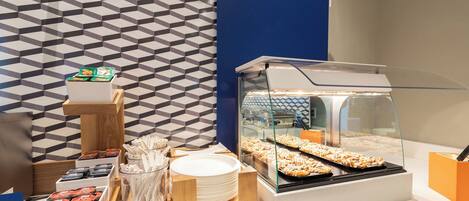 A buffet area with a display of cinnamon sweet rolls, a sign indicating the roll selection, and a patterned wall in the background.