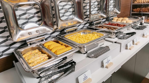 Un buffet proposant divers plats, notamment des œufs brouillés, une omelette au fromage et des saucisses de dinde.