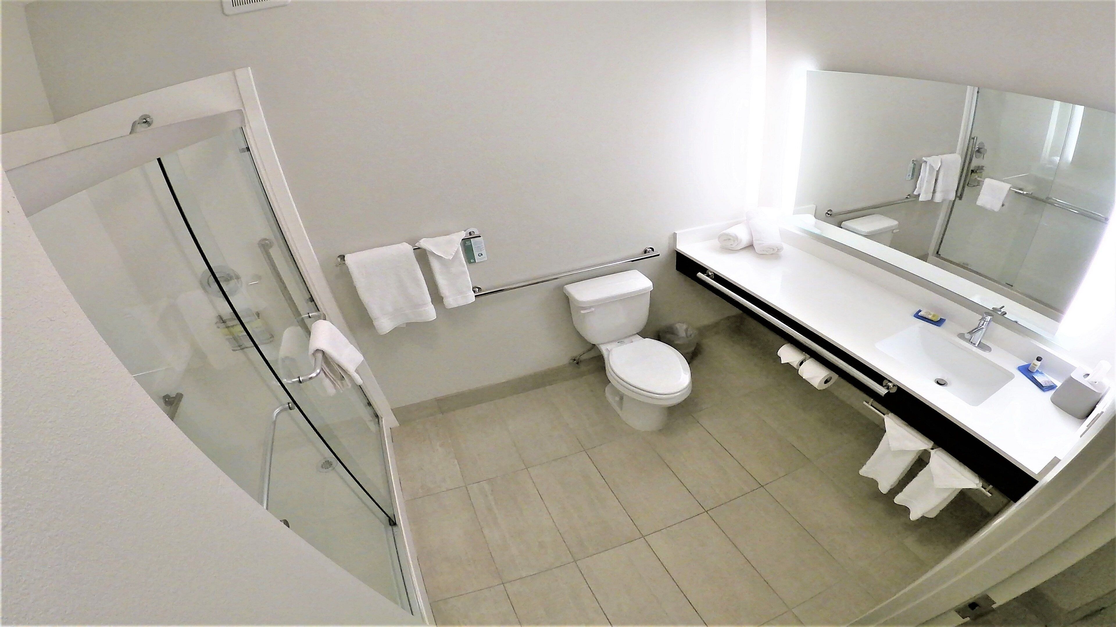 Une salle de bain moderne avec une douche à parois de verre, des toilettes, un lavabo avec un miroir et un porte-serviettes.