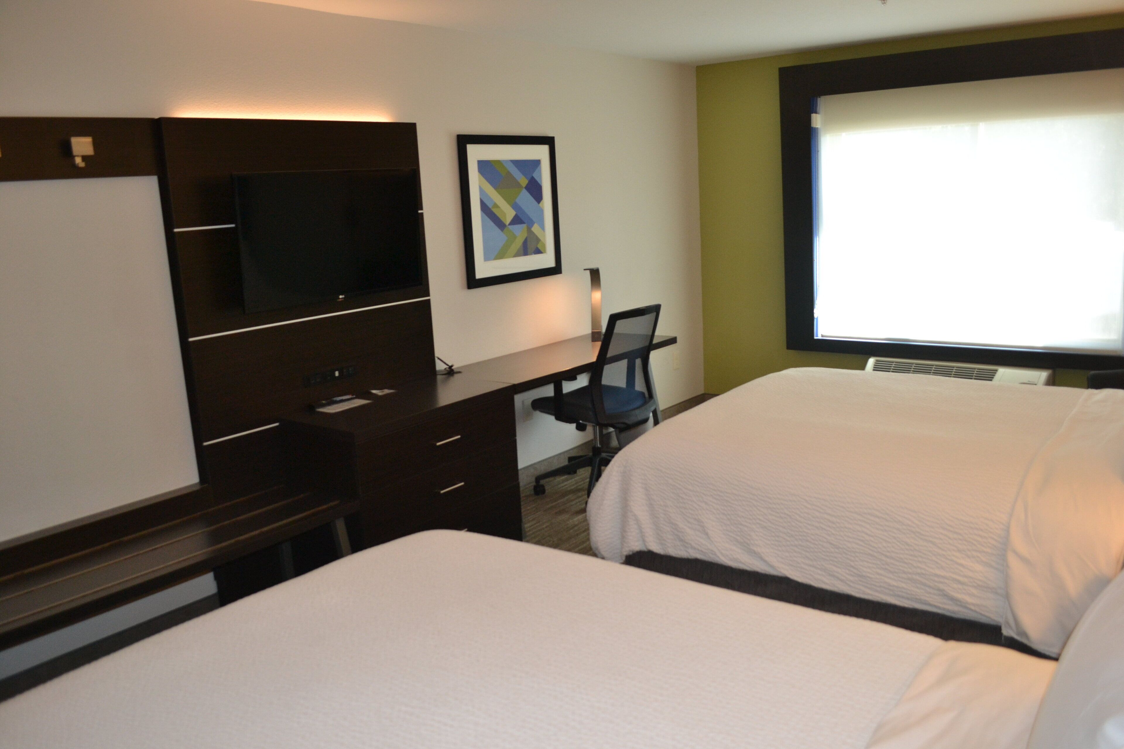 A hotel room with two beds, a desk with a chair, a television, and a framed picture on the wall.