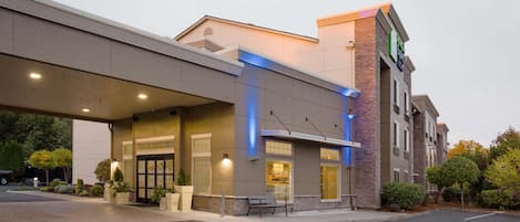 A hotel with a covered entrance, outdoor seating, and a brick facade.