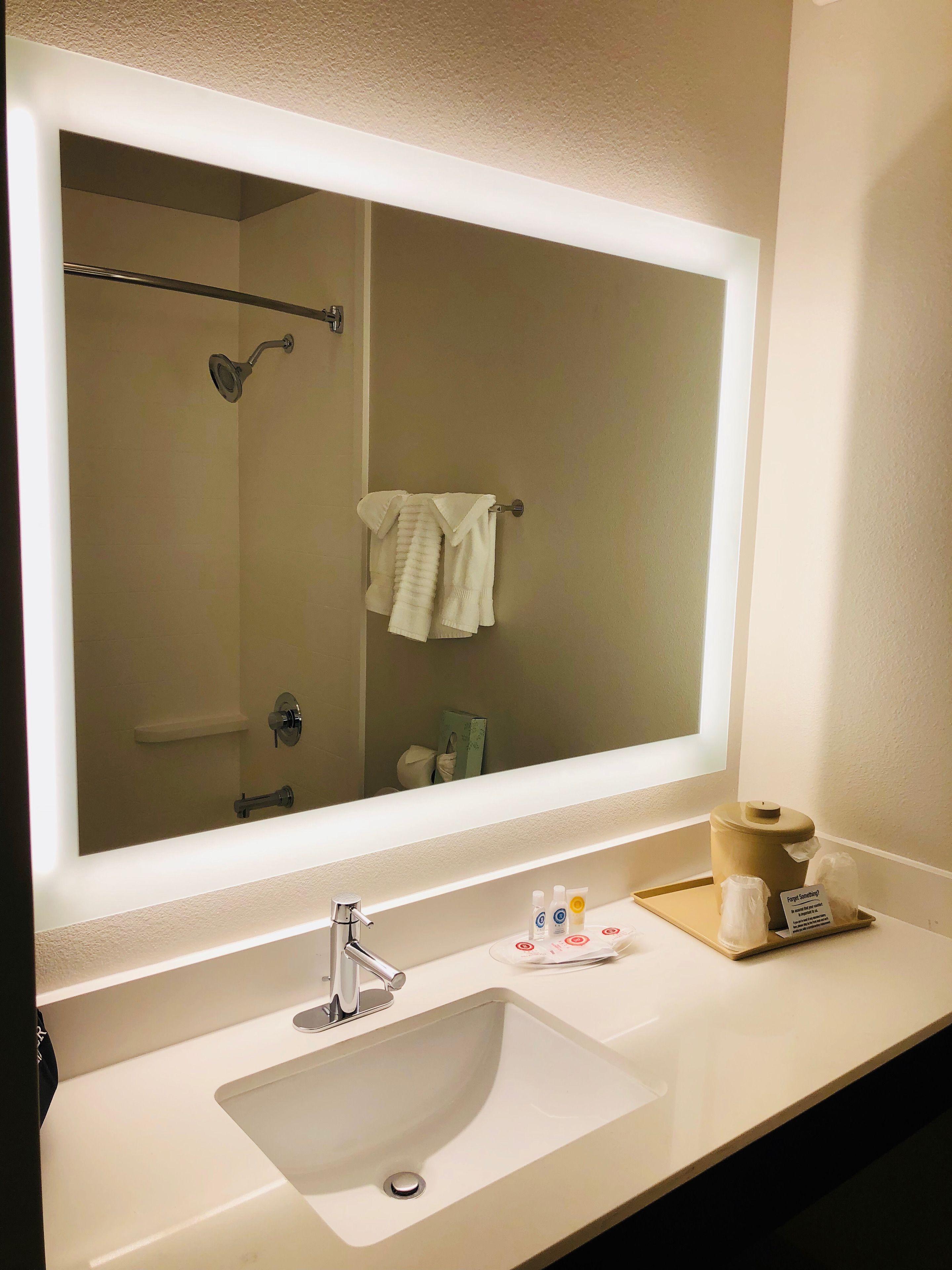 Ein Badezimmer mit einem großen Spiegel, einem Waschbecken und einem Handtuchhalter.