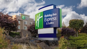 A Holiday Inn Express & Suites sign with a modern design, set against a backdrop of trees and a partly cloudy sky. - Holiday Inn Express & Suites Hood River by IHG (Hood River)