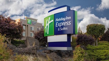 Placa do Holiday Inn Express & Suites com design moderno, com árvores e céu parcialmente nublado ao fundo.
