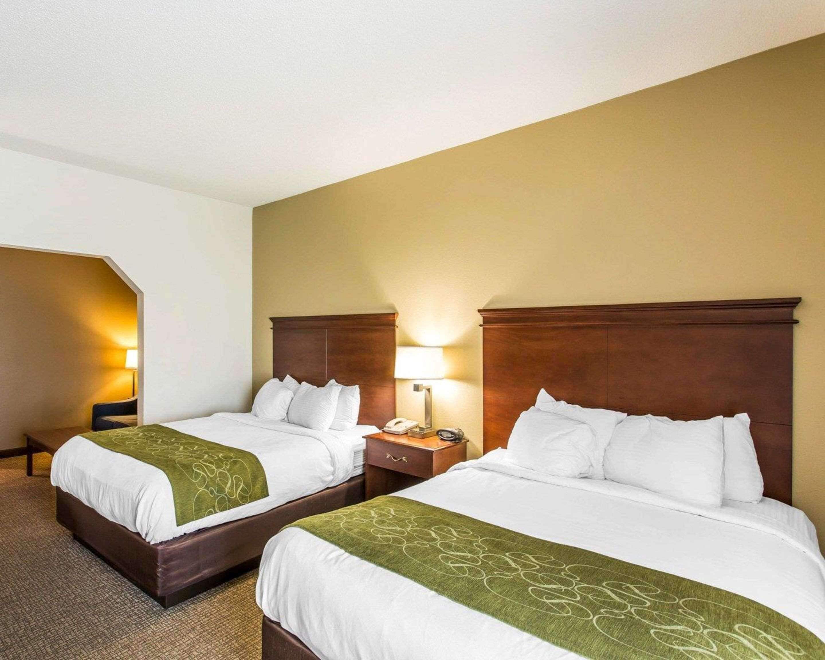 Habitación de hotel con dos camas, cada una con cabecero de madera, ropa de cama blanca y una manta verde. Hay lámparas de noche y un teléfono sobre las mesitas.