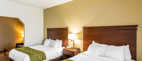 Habitación de hotel con dos camas, cada una con cabecero de madera, ropa de cama blanca y una manta verde. Hay lámparas de noche y un teléfono sobre las mesitas.