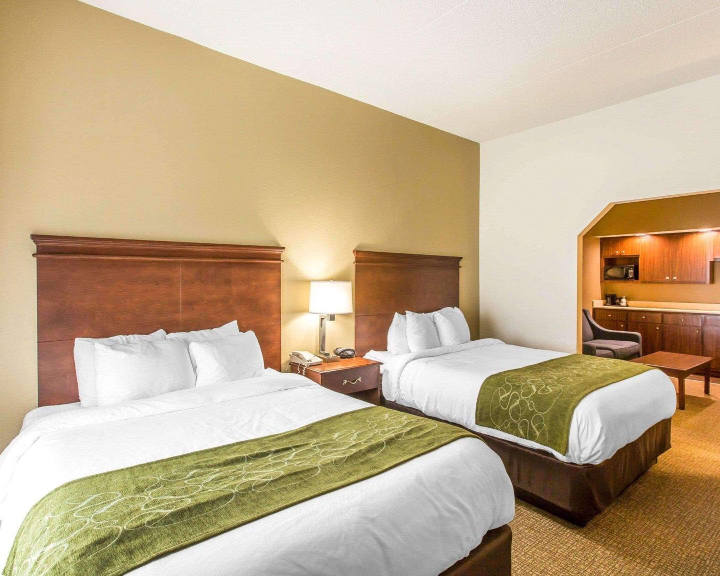 A hotel room with two beds, a small desk, a chair, and a kitchenette.