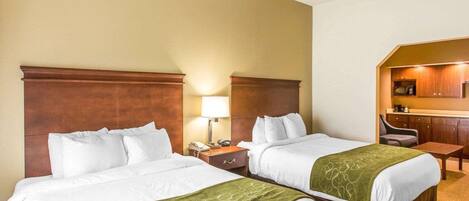 A hotel room with two beds, a small desk, a chair, and a kitchenette.