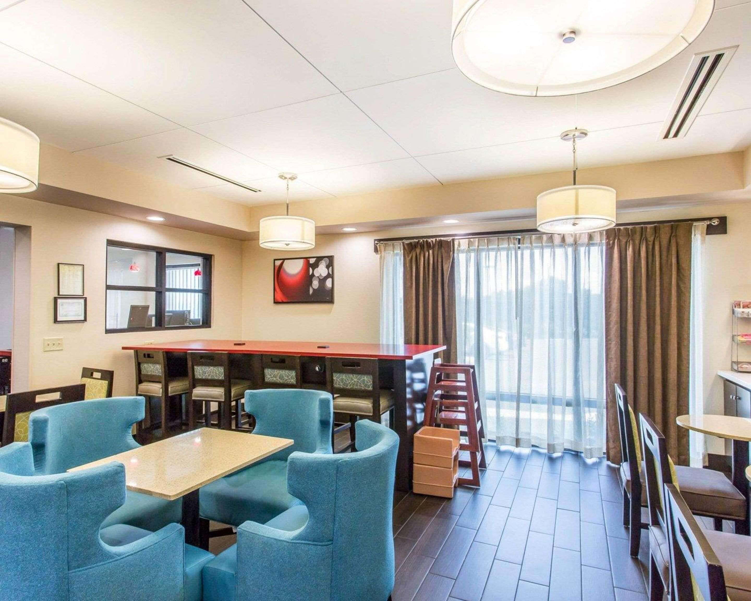 Ett hotellrum med en matplats som har ett långt bord och blå stolar, ett stort fönster med gardiner och ett tak med infälld belysning.