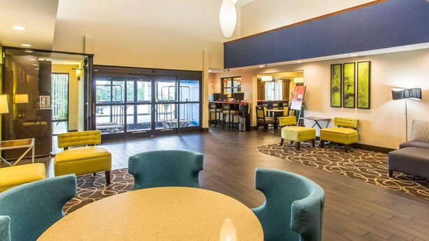 A spacious lobby with a round table, blue chairs, yellow ottomans, and a modern ceiling design.