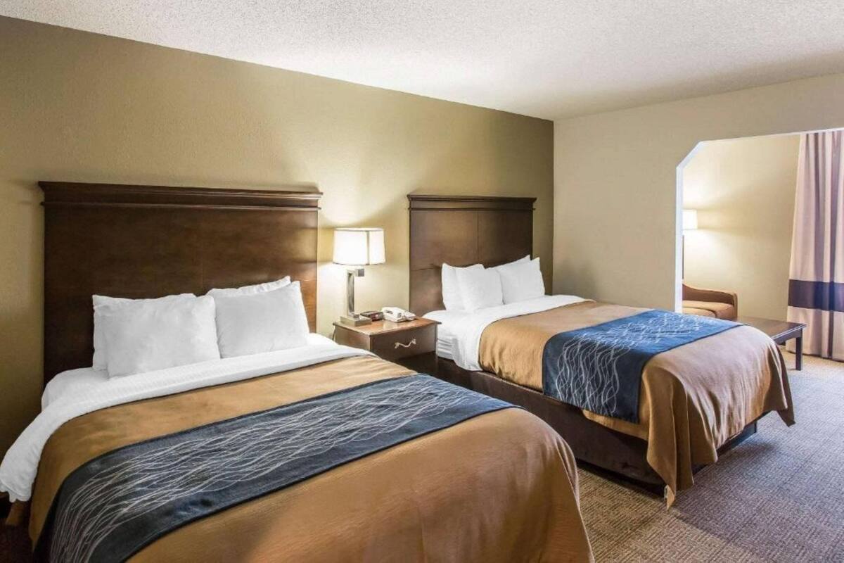 Une chambre d’hôtel avec deux lits, chacun doté d’une tête de lit en bois, d’une table de chevet avec une lampe et d’une fenêtre avec des rideaux.