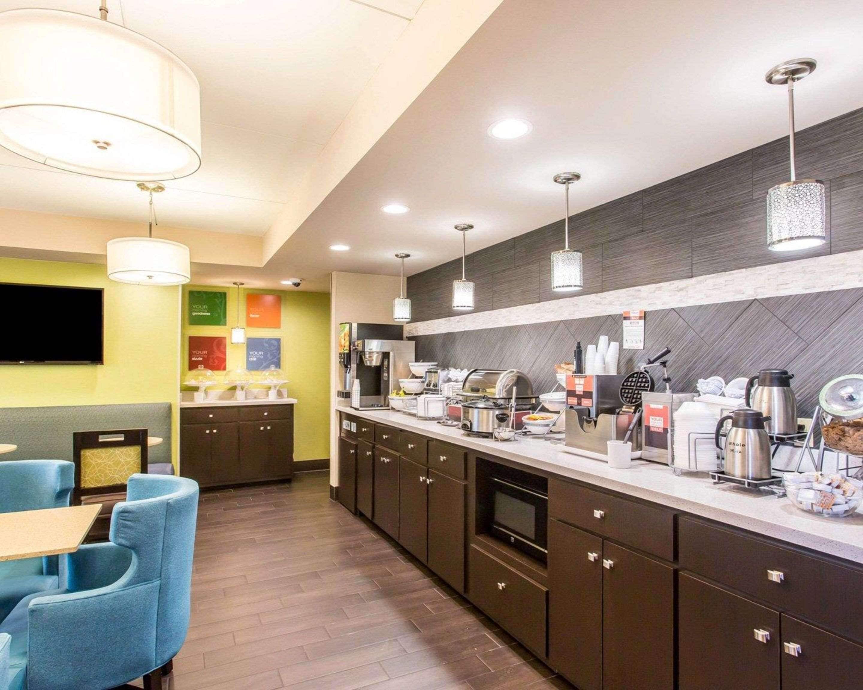 A modern kitchen with a long counter, built-in appliances, and a seating area with blue chairs.