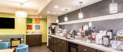 A modern kitchen with a long counter, built-in appliances, and a seating area with blue chairs.
