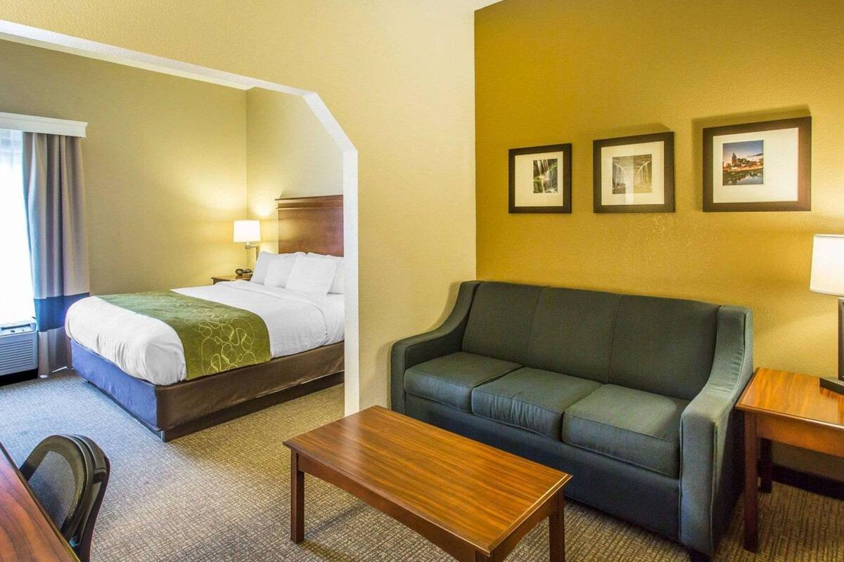 Une chambre d’hôtel avec un lit, un canapé, une table basse et un bureau. Trois tableaux encadrés sont accrochés au mur.
