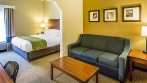 A hotel room with a bed, a sofa, a coffee table, and a desk. There are three framed pictures on the wall.
