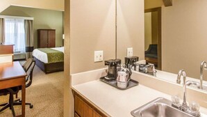 A hotel room with a bed, a desk, a chair, a coffee maker, a sink, and a large mirror.