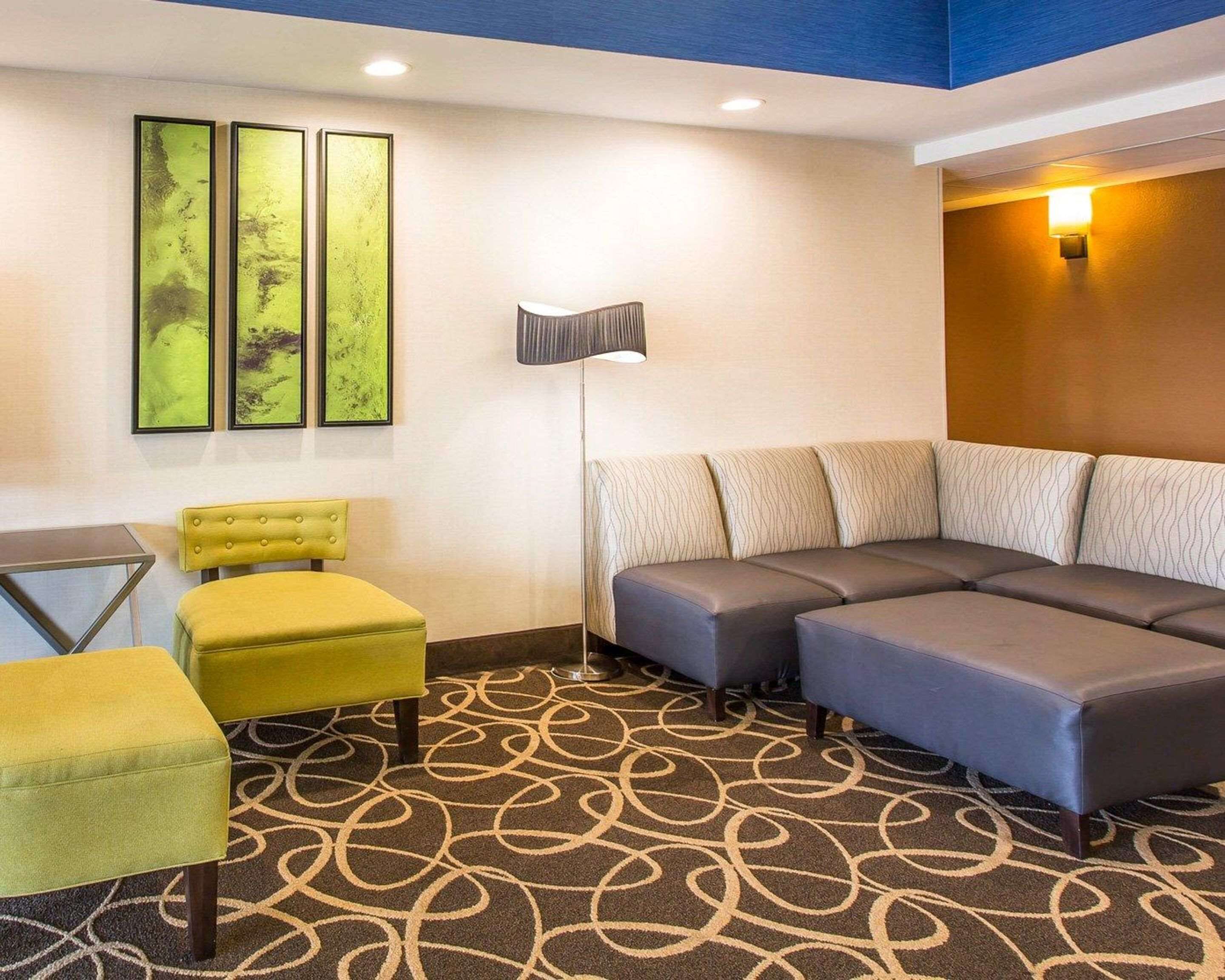 A hotel room with a sectional sofa, a yellow armchair, a floor lamp, and abstract art on the wall.