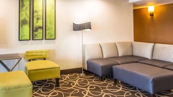 Habitación de hotel con sofá modular, un sillón amarillo, una lámpara de pie y arte abstracto en la pared.