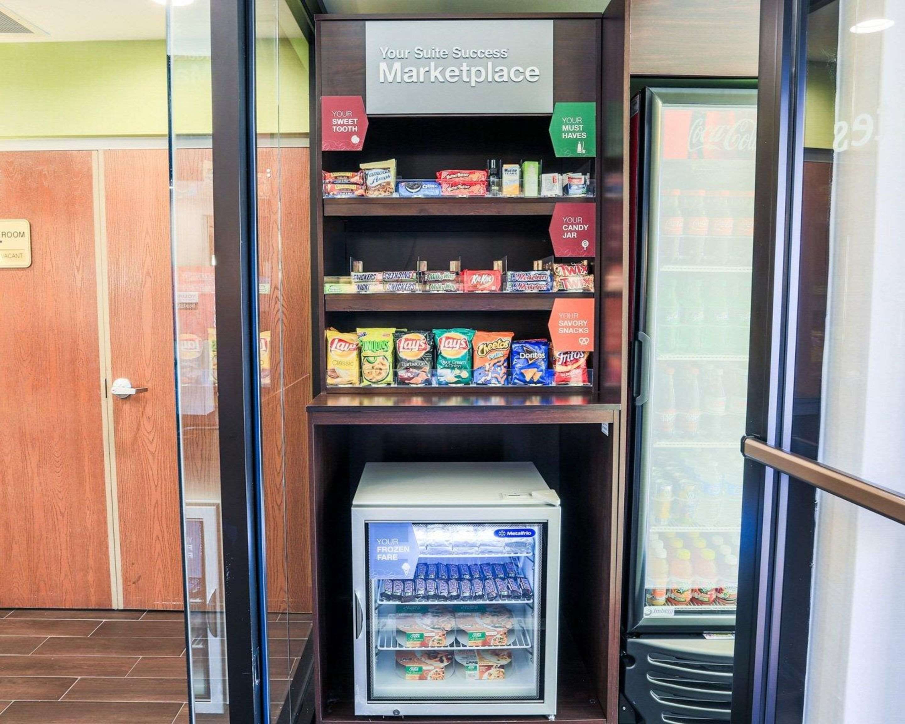 Un pequeño quiosco con bocadillos y un congelador, identificado como "Your Suite Success Marketplace", que exhibe diversas marcas de productos para el aperitivo.
