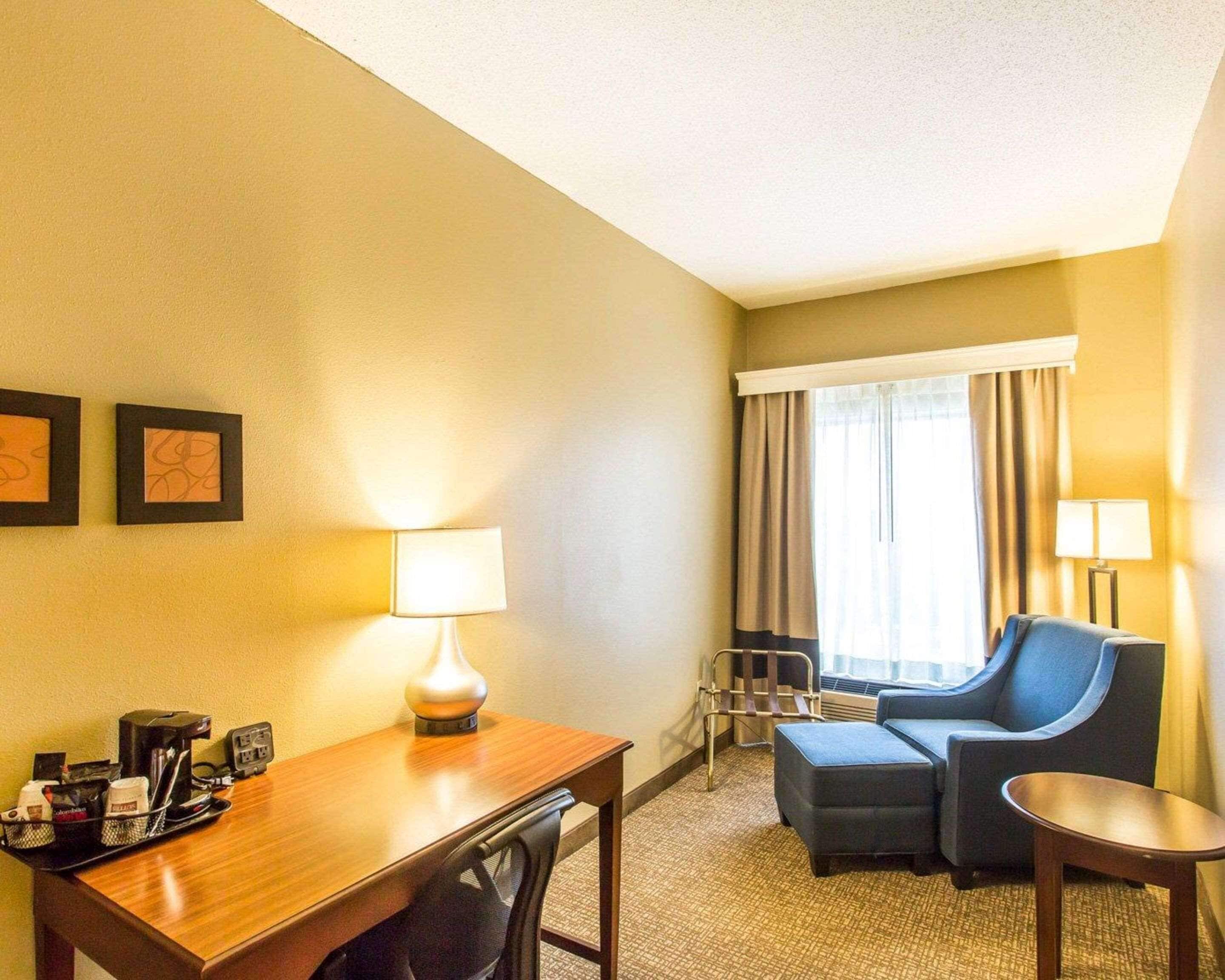 A hotel room with a wooden desk, two chairs, a sofa, a small table, and a window with curtains.