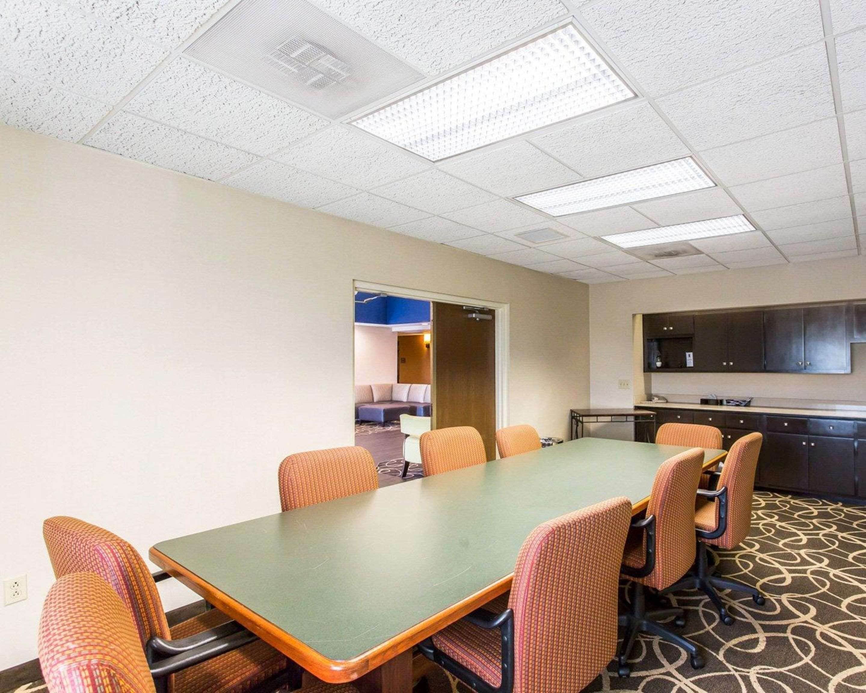 A conference room with a long table and six chairs, a kitchenette, and a door leading to a living area.