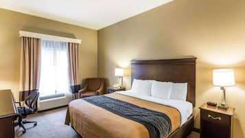 Camera d'albergo con un letto grande, una scrivania, una sedia, un condizionatore d'aria e un comodino con una lampada.