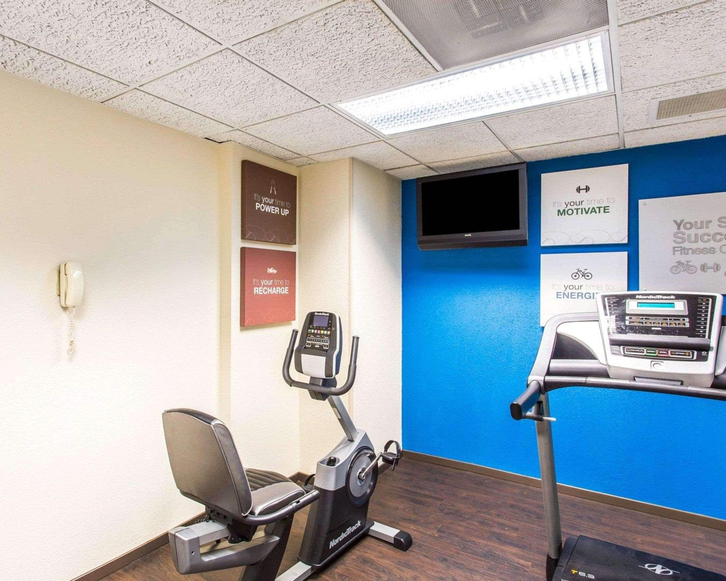 A fitness room with an elliptical machine, a treadmill, and motivational posters on the wall.