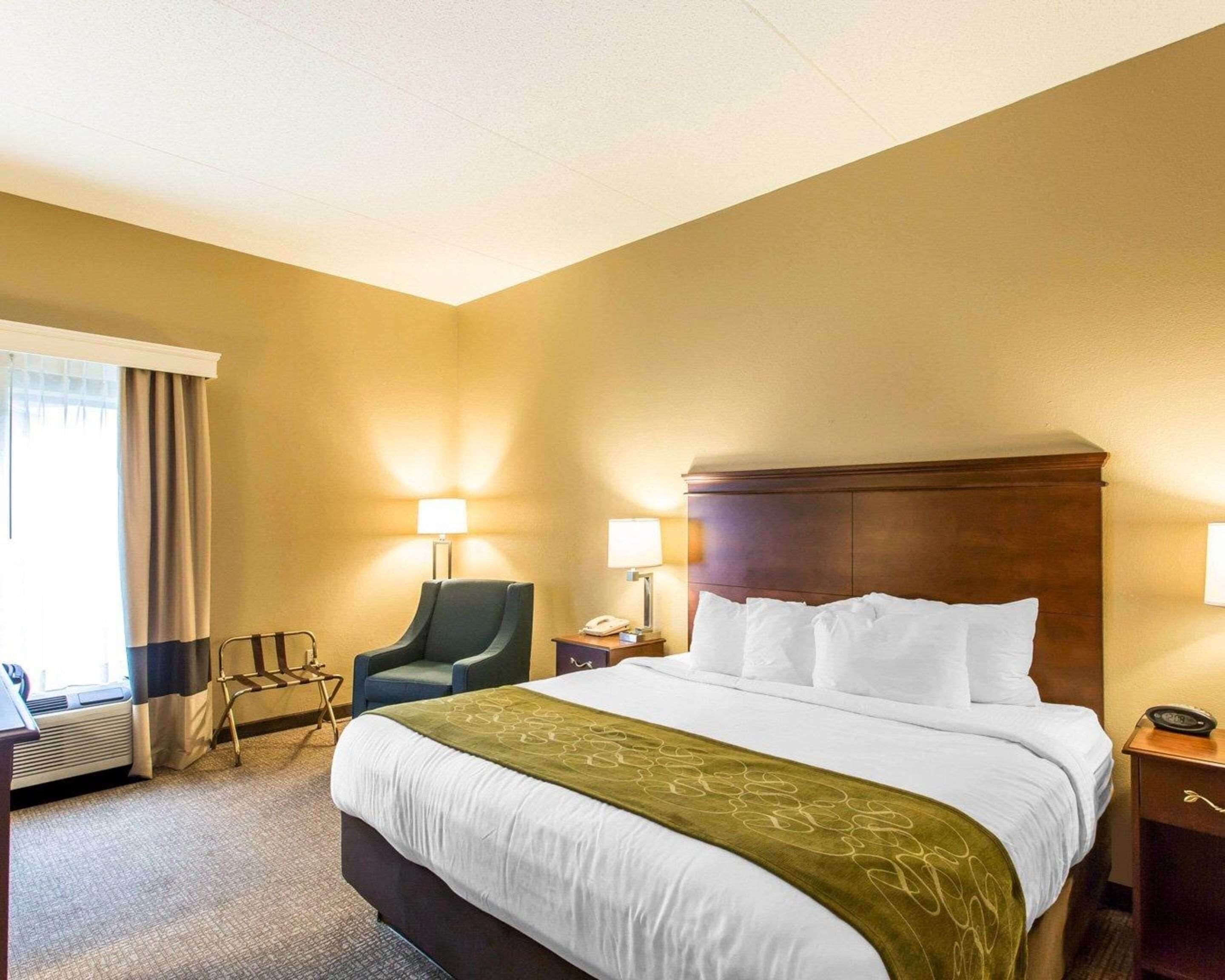 Habitación de hotel con una cama grande, dos lámparas de noche, una silla, un escritorio y una ventana con cortinas.