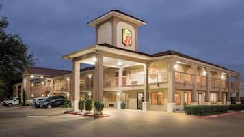 A hotel with a prominent Super 8 sign, multiple balconies, and a parking lot with several cars.