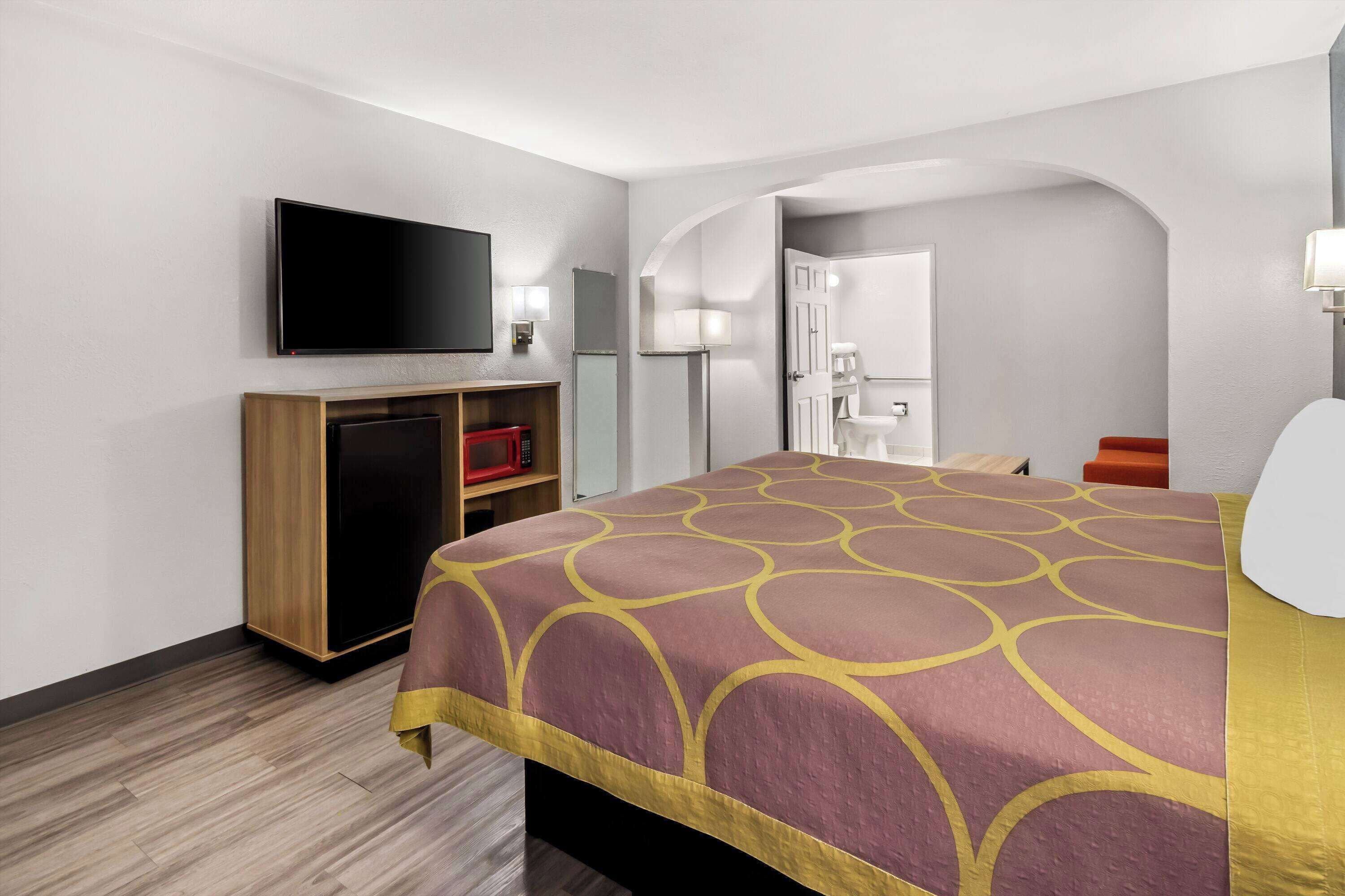 A hotel room with a large bed, a flat-screen TV mounted on the wall, a desk with a chair, and a wardrobe.