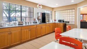 A kitchen with wooden cabinets, a white countertop, and orange chairs.