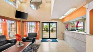 A hotel lobby with a reception desk, seating area, and large windows with orange curtains.