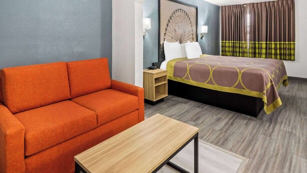 A hotel room with a bed, orange sofa, wooden nightstand, and a small table.