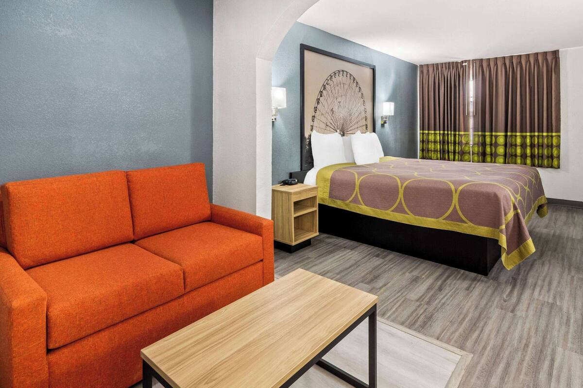 Een hotelkamer met een bed, een oranje bank, een houten nachtkastje en een kleine tafel.