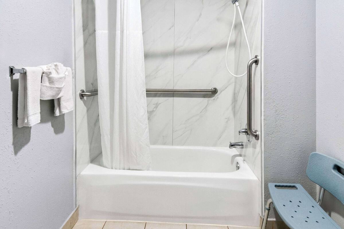 Een badkamer met een wit bad, douchegordijn, een greep, handdoekhouder en een blauwe bank.