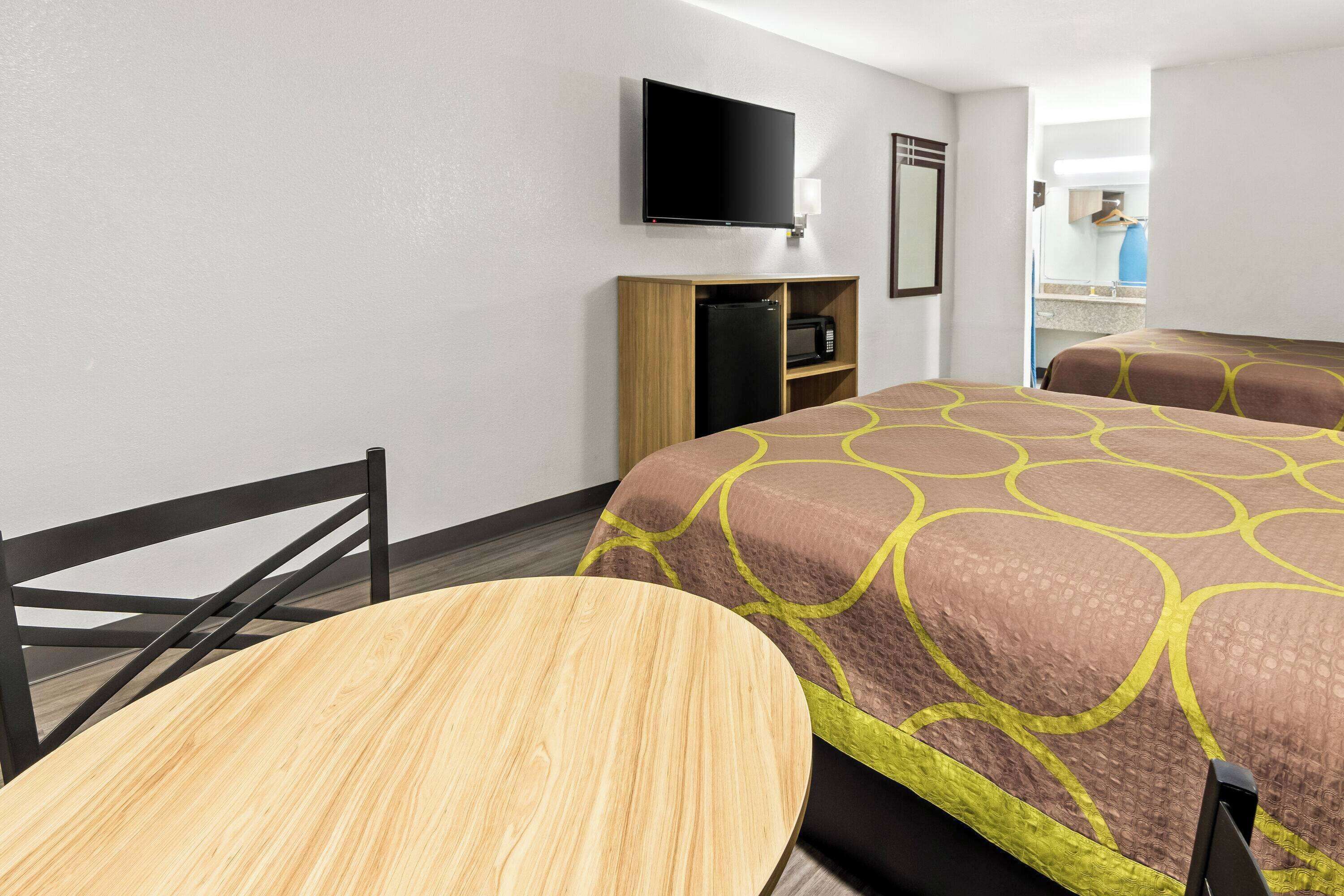 Ein Hotelzimmer mit Bett, Wandfernseher, einer kleinen Küchenzeile und einem Holztisch.