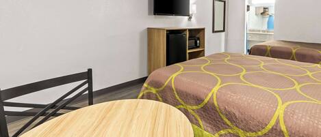 Habitación de hotel con cama, televisor montado en la pared, kitchenette pequeña y una mesa de madera.
